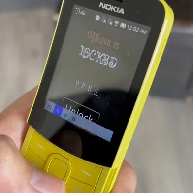 Old yellow Nokia phone that shows a screen reading "Trunk is locked" and a password getting typed in